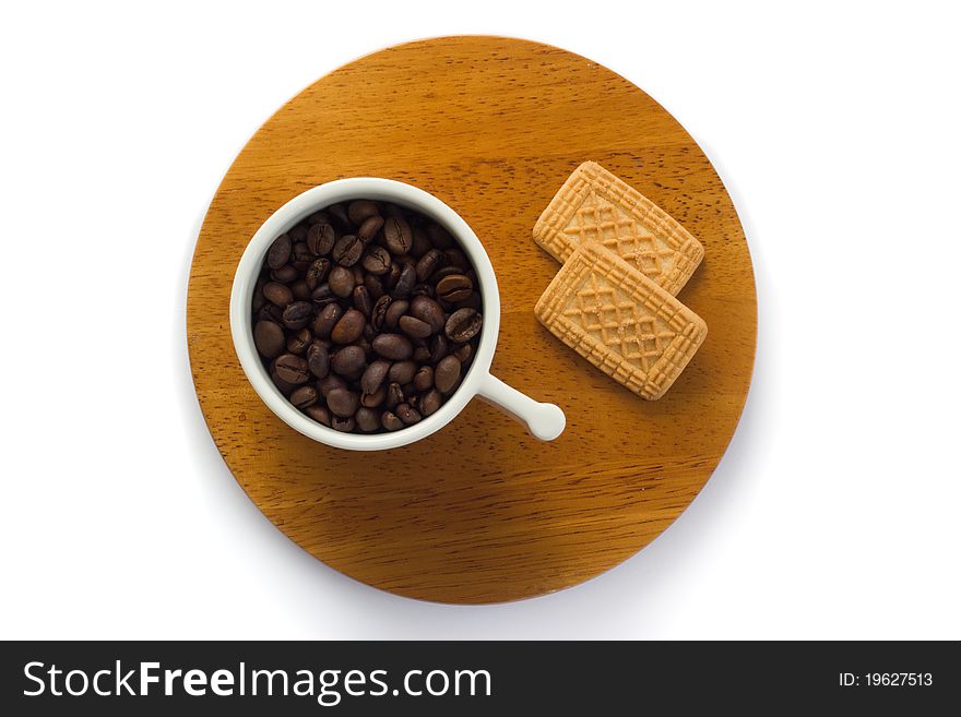 White ceramic cup of coffee beans on wooden sauce rwith two biscuits, isolated on white.