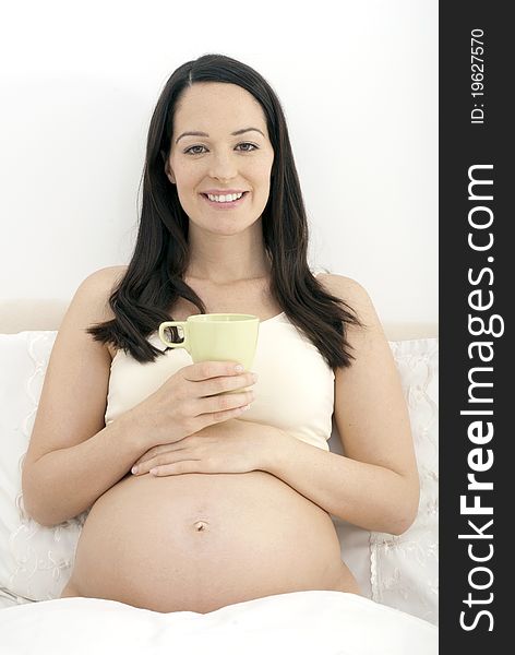 Pregnant woman in bed holding mug of tea. Pregnant woman in bed holding mug of tea
