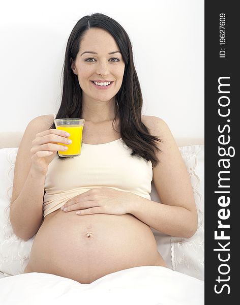 Pregnant woman in bed drinking a glass of orange juice smiling to camera. Pregnant woman in bed drinking a glass of orange juice smiling to camera