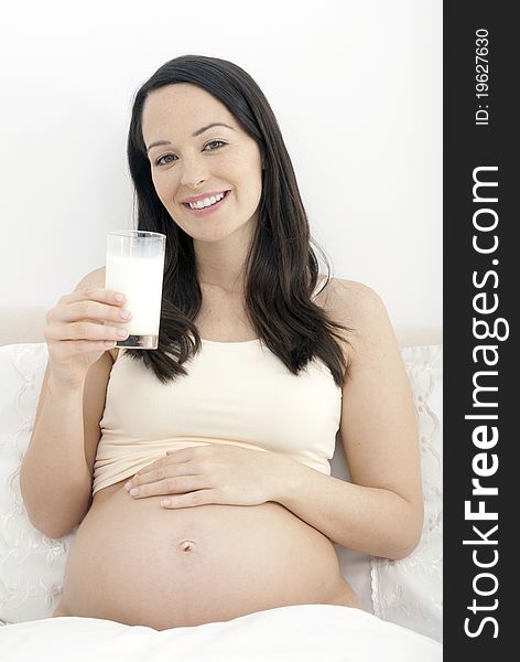 Pregnant woman in bed drinking a glass of milk smiling to camera. Pregnant woman in bed drinking a glass of milk smiling to camera