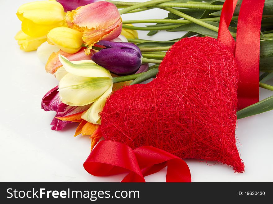 Lovely spring colored tulips with water drops lie in the bouquet in the foreground of the red heart. Isolated. Lovely spring colored tulips with water drops lie in the bouquet in the foreground of the red heart. Isolated