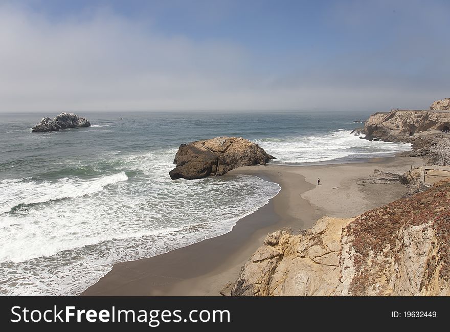 Lone person on beach with brown boulders and blue ocean all around. Lone person on beach with brown boulders and blue ocean all around.