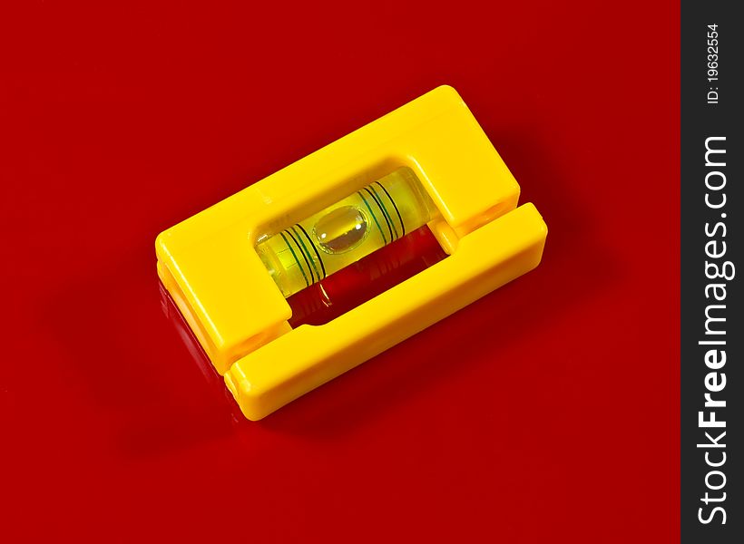 A small yellow plastic, bubble level l on a red background