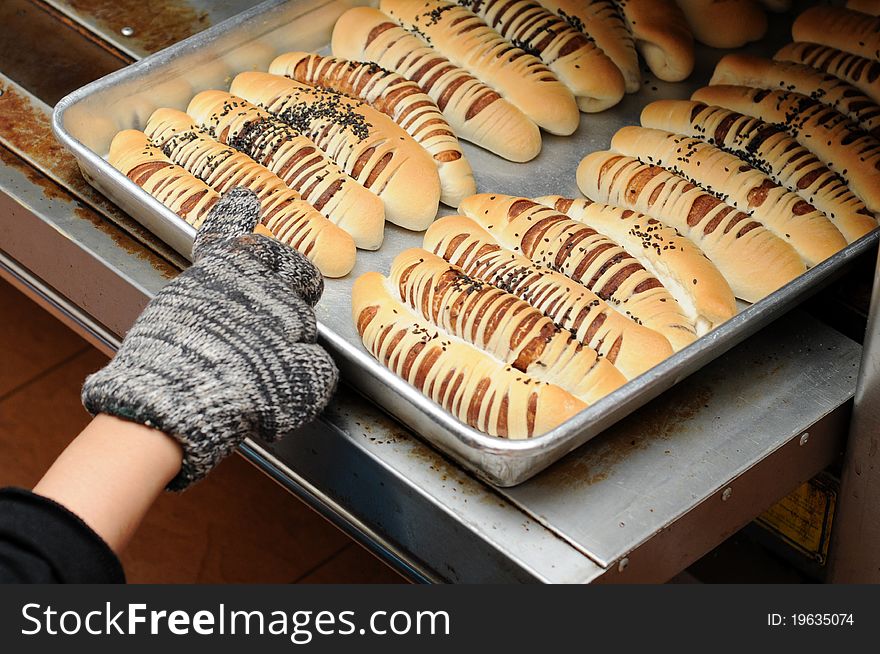 Hand pull out baked bread on tray. The hand wear gloves.