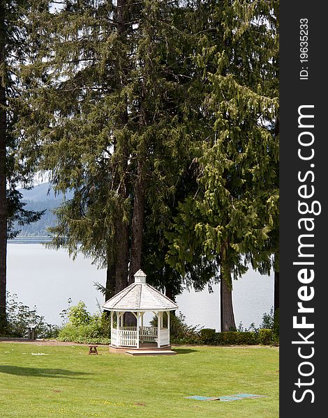 A white gazebo set on a lake backed by pine trees