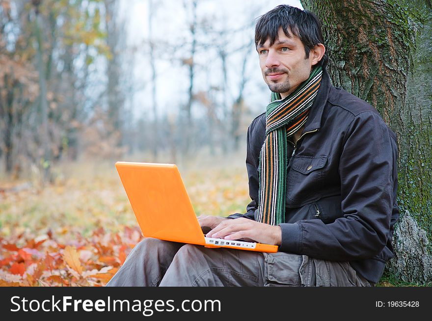 Romantic young man sitting with laptop in the autumn park. Romantic young man sitting with laptop in the autumn park.