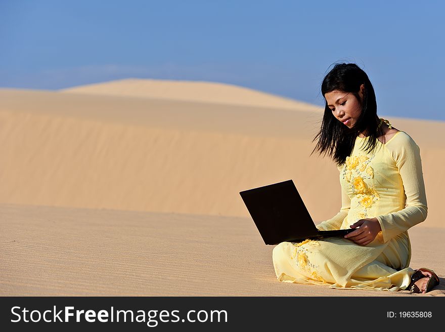 Young Asian woman with a laptop in the dunes. Young Asian woman with a laptop in the dunes