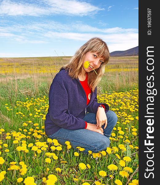 Smiling beautiful girl sitting on a dandelions field with dandelion in her mouth. Smiling beautiful girl sitting on a dandelions field with dandelion in her mouth