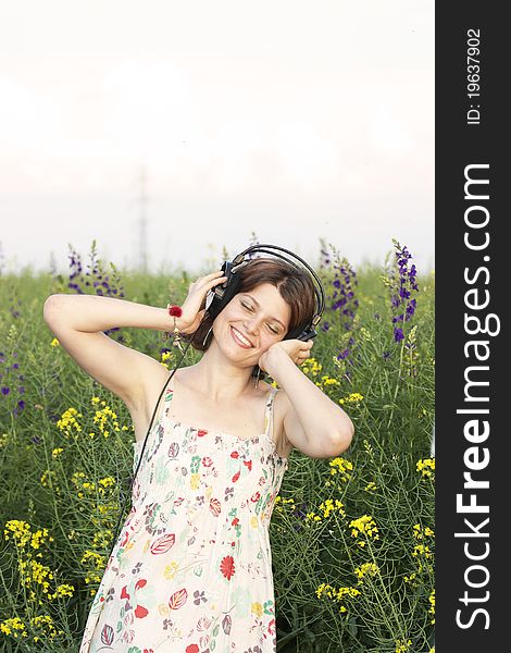 Portrait of girl who listening music in ear-phones on a field of flowers. Portrait of girl who listening music in ear-phones on a field of flowers