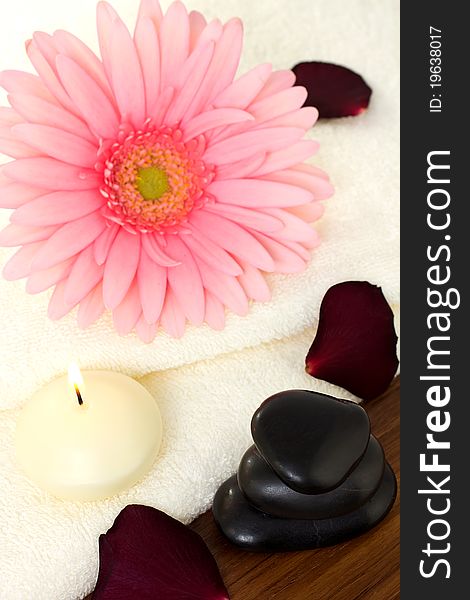 Aromatherapy relaxation, bath towels and a pink flower with a candle and massage stones.