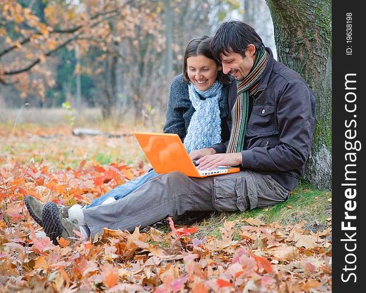 Romantic mature couple sitting with laptop in the autumn park. Romantic mature couple sitting with laptop in the autumn park.