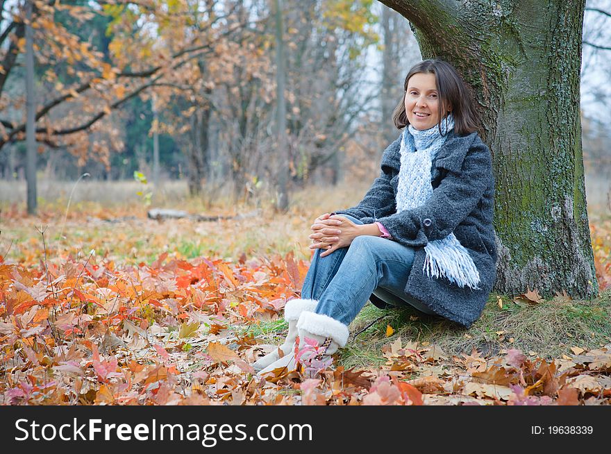 Cute happy young woman sitting in the autumn park. Cute happy young woman sitting in the autumn park.