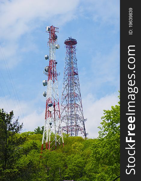 Cell phone and communication towers against blue sky with scattered clouds