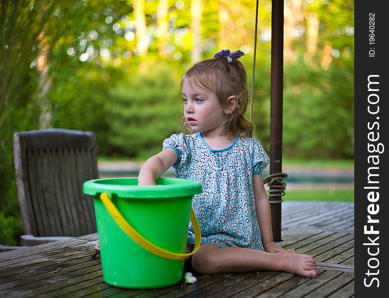 Young Girl Playing With A Bucket On A Teak Patio Table. Young Girl Playing With A Bucket On A Teak Patio Table