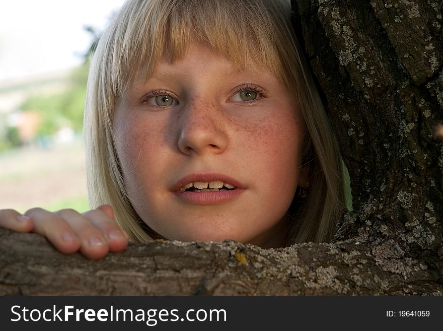 The young girl with freckles looking out because of a tree