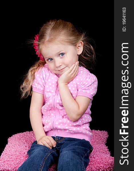 A photograph of a cute girl sitting on a pink pillow. A photograph of a cute girl sitting on a pink pillow.