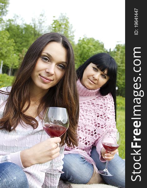 Mother and daughter sitting at a picnic on a blanket drinking wine. Mother and daughter sitting at a picnic on a blanket drinking wine