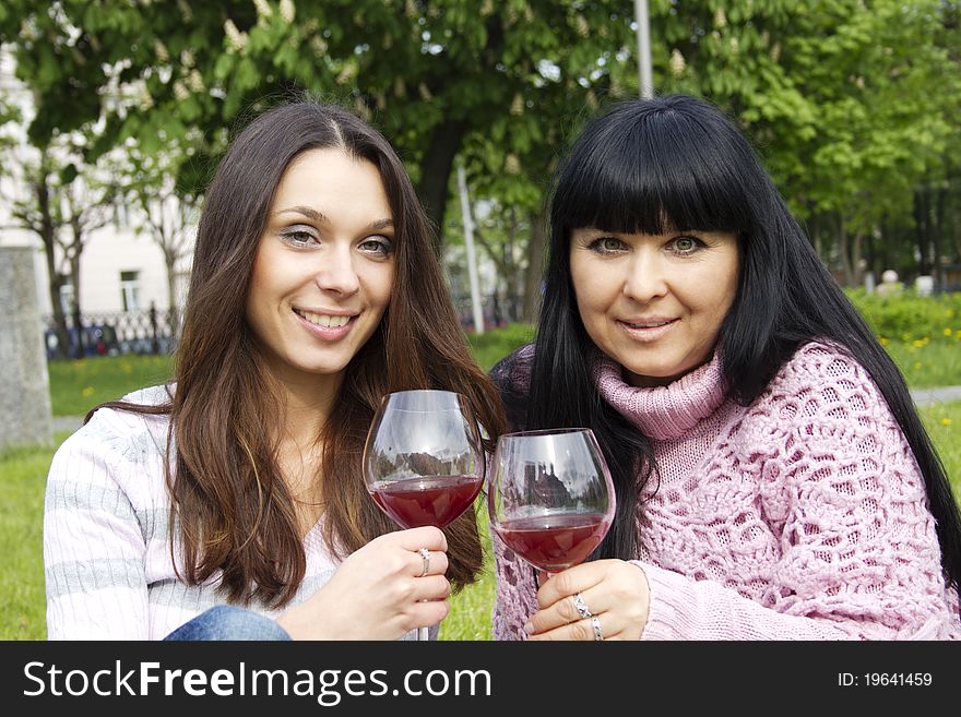 Mother and daughter sitting at a picnic on a blanket drinking wine. Mother and daughter sitting at a picnic on a blanket drinking wine