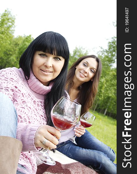 Mother and daughter sitting at a picnic on a blanket drinking wine. Mother and daughter sitting at a picnic on a blanket drinking wine