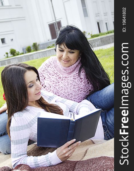 Attractive Mom and daughter, a teenager in a park reading a book and make merry. Attractive Mom and daughter, a teenager in a park reading a book and make merry