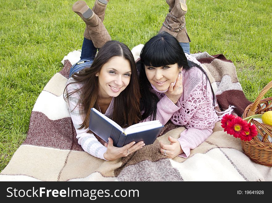 Attractive Mom and daughter, a teenager in a park reading a book and make merry. Attractive Mom and daughter, a teenager in a park reading a book and make merry