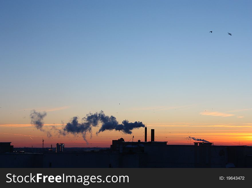 At sunset from a town house pipe there is a smoke. At sunset from a town house pipe there is a smoke