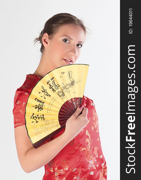 The beautiful young girl in a red Chinese dress with a yellow fan in hands. The beautiful young girl in a red Chinese dress with a yellow fan in hands