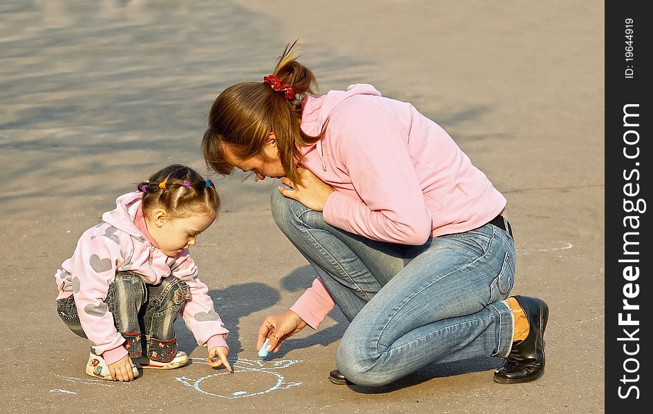 The child with mum draw a chalk on asphalt
