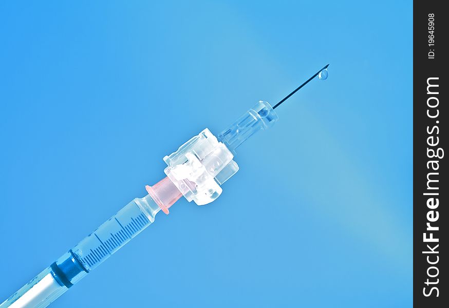 Syringe on blue background with drop of medicine on the needle. Syringe on blue background with drop of medicine on the needle