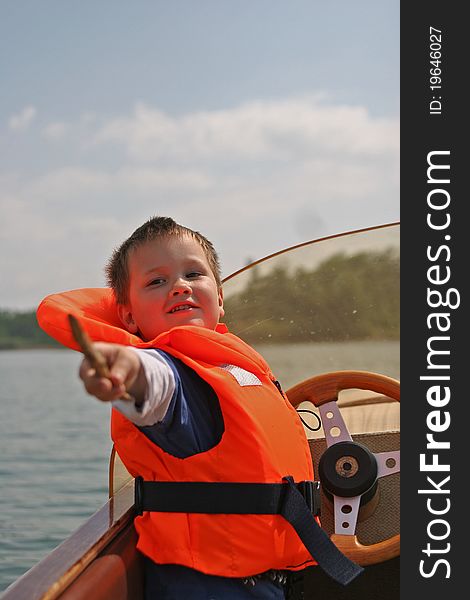 Young caucasian white boy in life jacket on a boat in front of the steering wheel. Young caucasian white boy in life jacket on a boat in front of the steering wheel