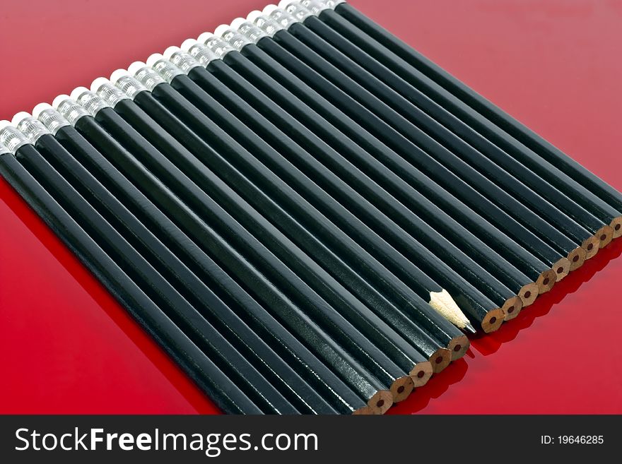 a background of a single sharp black lead pencil in a row of unsharpened pencils. a background of a single sharp black lead pencil in a row of unsharpened pencils