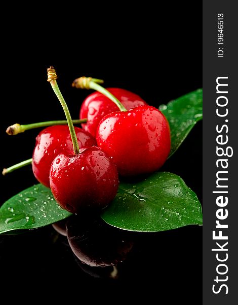 Photo of delicious wet cherries on green leaves over black reflecting background
