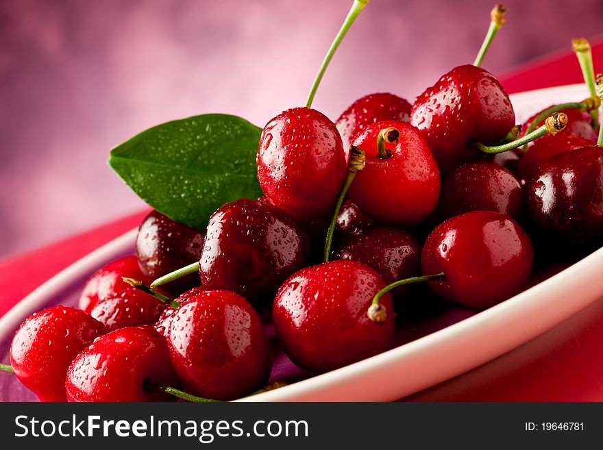 Photo of delicious fresh cherries inside a plate on red reflecting table. Photo of delicious fresh cherries inside a plate on red reflecting table