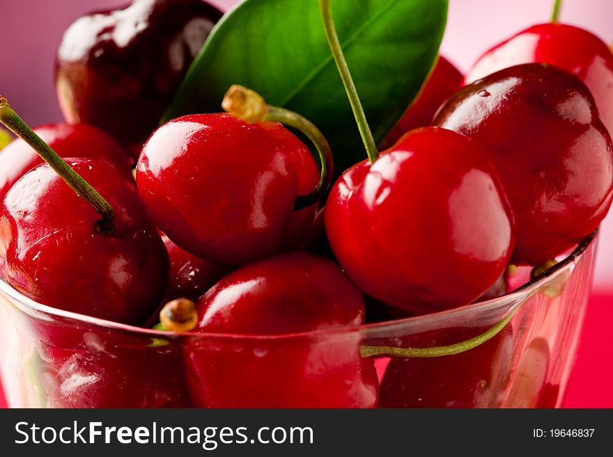 Photo of delicious fresh cherries inside a glass on red highlighted background. Photo of delicious fresh cherries inside a glass on red highlighted background
