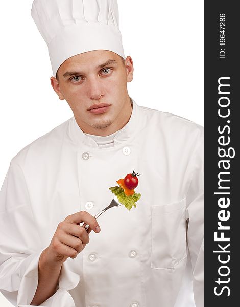 The young chef in uniform and chef's hat holding a fork and vegetables.