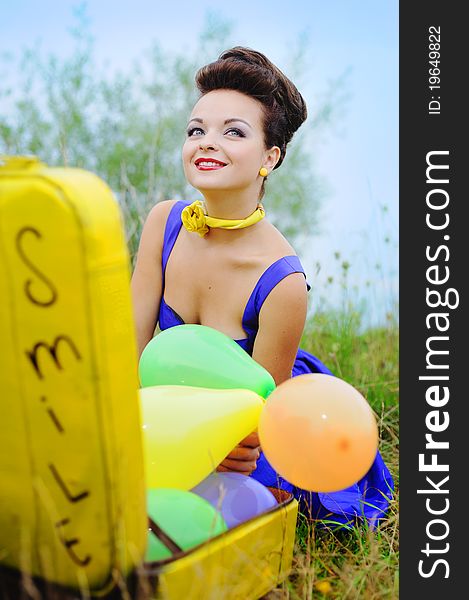 Beautiful smiling girl in a blue dress with a yellow suitcase and colorful balloons. Beautiful smiling girl in a blue dress with a yellow suitcase and colorful balloons