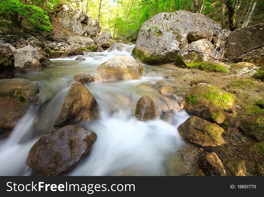 The mountain river in gorge with a spring with dim water and bright foliage of trees on a background. A landscape.