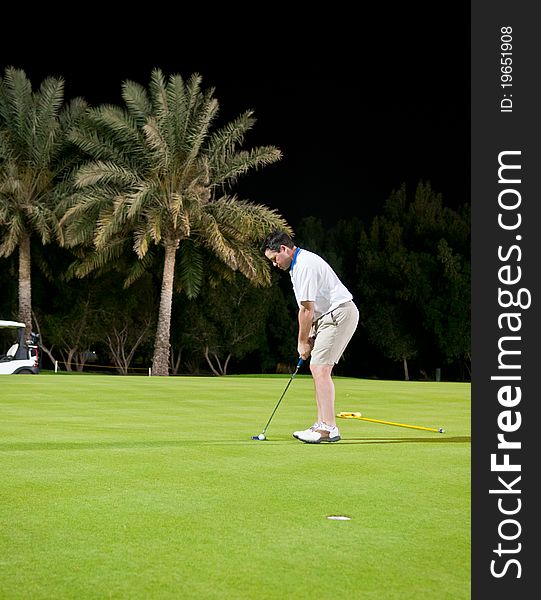 A male golfer prepares to putt the ball in the hole during a night game. A male golfer prepares to putt the ball in the hole during a night game.