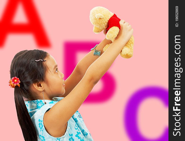 Girl Holding Her Teddy Bear Up In The Air - In Her Playroom With ABC Background