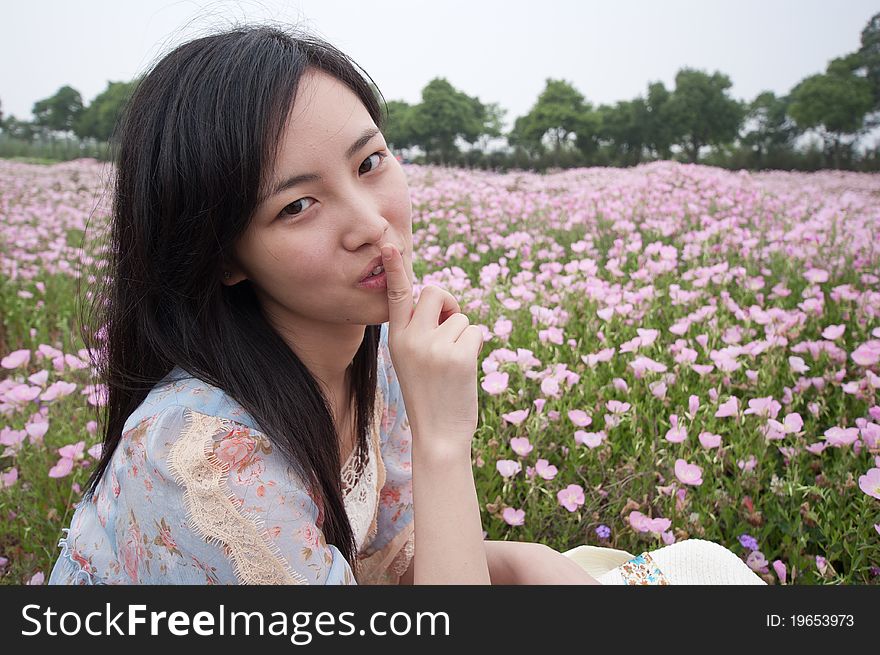 A girl doing silence gesture in field with flowers around. A girl doing silence gesture in field with flowers around