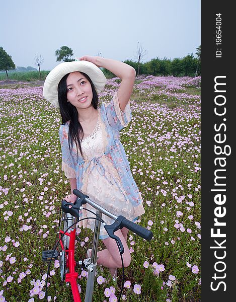 A girl wearing a capeline is playing in flower field with bike. A girl wearing a capeline is playing in flower field with bike