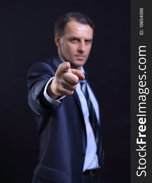 Closeup portrait of a young business man pointing at the camera on a dark background