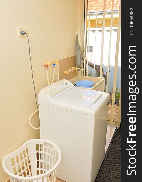 Interior of washing area with white washing machine and laundry basket.