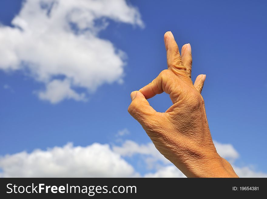 Hand showing okay sign on right of frame with blue sky and cloud background. Hand showing okay sign on right of frame with blue sky and cloud background.