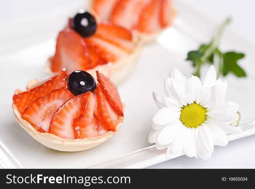 Piece of cake on plate with berries and fruits and camomile