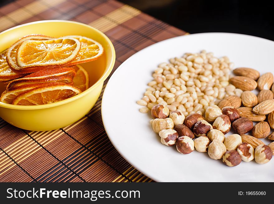 Mixed nuts on a white plate and dried orange