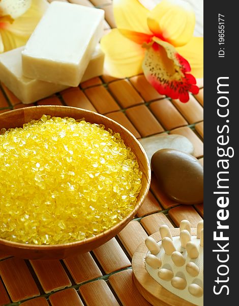 Spa composition of yellow bath salt in wooden bowl, soap and flowers