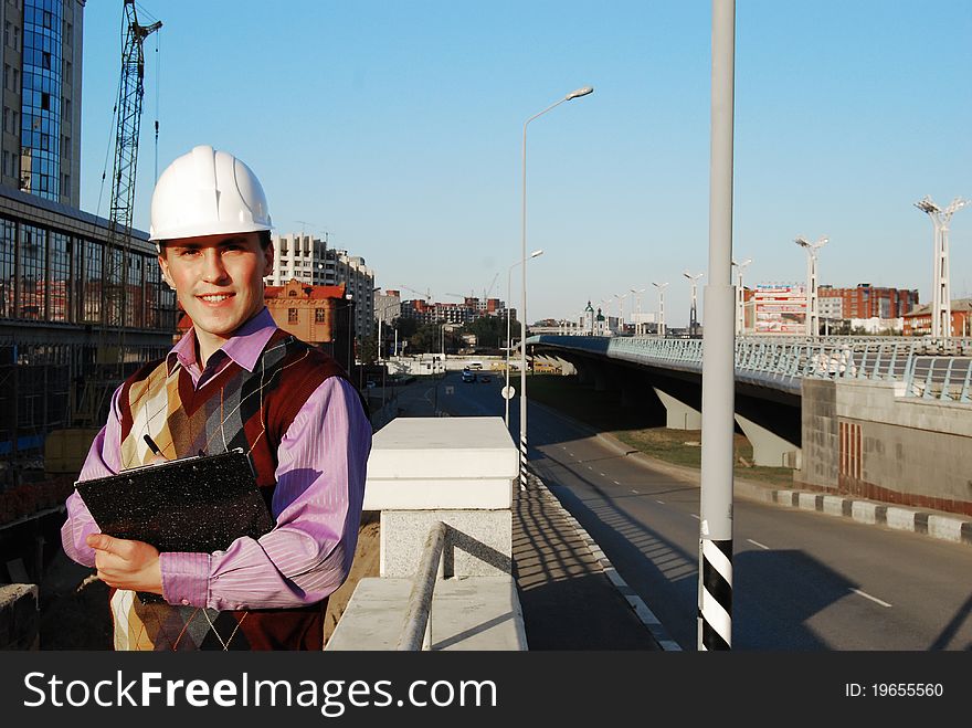 Industrial theme: architect, on a workplace, in a warm winter jacket and a helmet, has control over a tablet. Industrial theme: architect, on a workplace, in a warm winter jacket and a helmet, has control over a tablet.