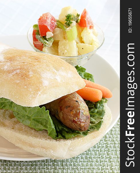 Spicy sausage on a ciabatta bun served with a side of potato salad. Spicy sausage on a ciabatta bun served with a side of potato salad