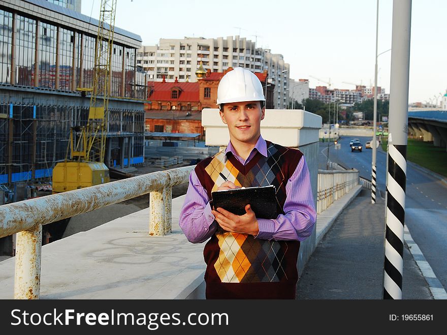 Industrial theme: architect, on a workplace, in a warm winter jacket and a helmet, has control over a tablet. Industrial theme: architect, on a workplace, in a warm winter jacket and a helmet, has control over a tablet.